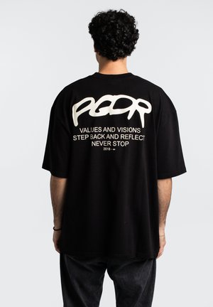 Black oversized t-shirt with short sleeves. Features white text on back: "PGDR" and phrases. Made of cotton fabric, simple design, relaxed fit.