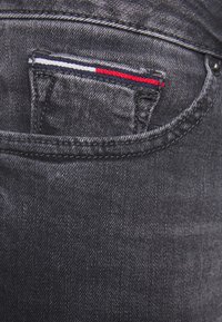 Jeans de mezclilla oscura con un pequeño bolsillo que presenta rayas rojas, blancas y azules; tejido texturizado con un patrón de costura clásico.