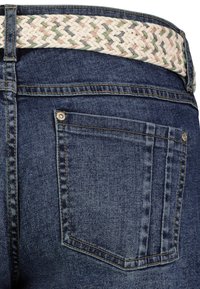 Jeans aus Denim mit blauer Waschung, Gesäßtasche und einem geflochtenen Woven-Gürtel in Beige, Grün und Pink. Genähte Details an den Nähten.