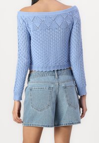 Ljusblå stickad off-shoulder-tröja med texturerat diamantmönster, kort design och ribbade manschetter, ihop med högmidjade denimshorts.