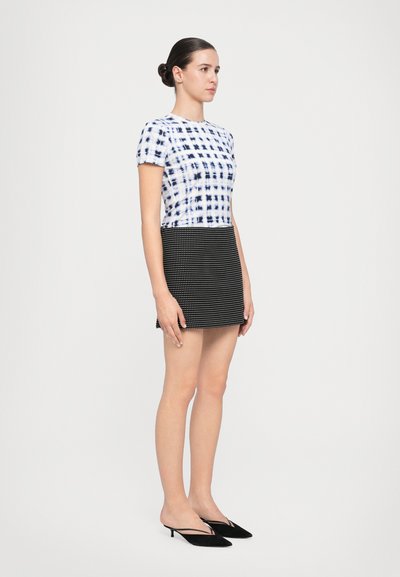 Short-sleeve top with blue and white plaid design, paired with a black mini skirt featuring a textured pattern. Black pointed-toe heels.