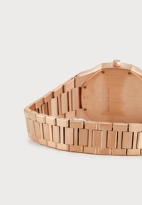 Roségoldene Uhr mit einem oktagonalen Gehäuse und einem Metallarmband, das eine Kombination aus polierten und gebürsteten Texturen aufweist.