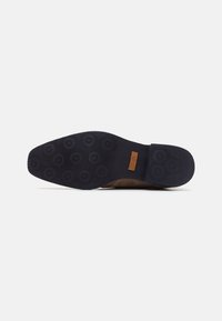 Sole di scarpa in pelle marrone con un fondo in gomma blu scuro testurizzato. Presenta motivi circolari per una migliore aderenza e una piccola etichetta beige con la scritta "M&H".