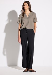 Blusa verde oliva con scollatura a V e maniche corte, abbinata a pantaloni larghi a coste neri e scarpe piatte in tessuto intrecciato. Design semplice e funzionale.