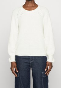 Valkoinen neulepusero, jossa pyöreä pääntie, resorit hihansuuissa ja teksturoitu pinta. Yhdistetty tummansinisiin cargo-farkkuihin.