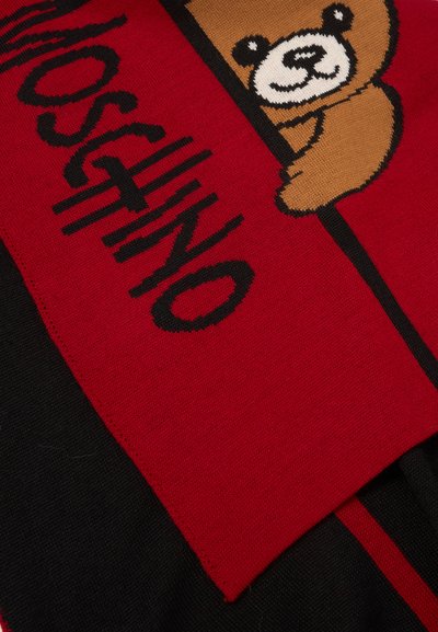 Tissu rouge et noir avec un graphique d'ours en peluche marron et le mot "MOSCHINO" en lettres noires et grasses sur la partie rouge.