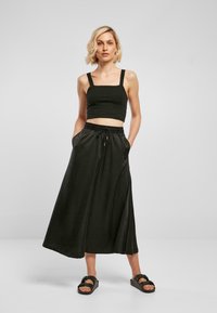 Svart crop top med brede stropper, kombinert med et langt, flytende svart skjørt med snøring i midjen og lommer. Sandaler fullfører antrekket.