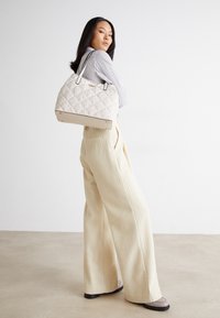 Beżowa pikowana torebka z dekoracyjnymi wzorami, zaokrąglonymi krawędziami, podwójnymi uchwytami i złotym wykończeniem; zestawiona z kremowymi, szerokimi spodniami.