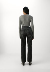 Maglietta grigia a maniche lunghe a costine abbinata a jeans in denim neri a vita alta. I jeans hanno un taglio classico con tasche posteriori e una finitura strutturata.