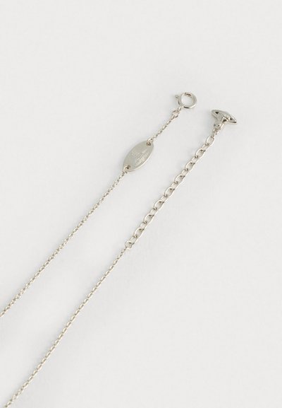 Dos cadenas de plata con diferentes estilos de eslabones, cada una con un cierre redondo y un pequeño charm ovalado con un símbolo grabado.