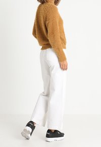 Maglione marrone soffice con maniche lunghe abbinato a jeans bianchi a gamba larga e sneakers nere. Texture notevole e vestibilità ampia.