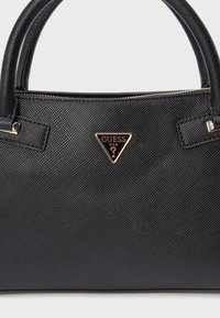 Borsa nera testurizzata con chiusura a cerniera, doppi manici e dettaglio logo triangolare in tonalità oro. Il materiale ha una finitura resistente.