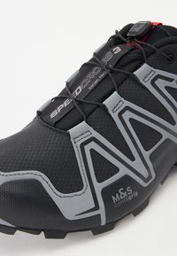 Black trail shoe featuring a textured mesh upper, grey accents, and a streamlined design with a quick-lacing system. M&S Contagrip logo visible.