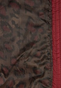 Tissu marron foncé avec un motif léopard noir et rouge foncé, à côté d'un panneau vertical en tissu rouge foncé matelassé.