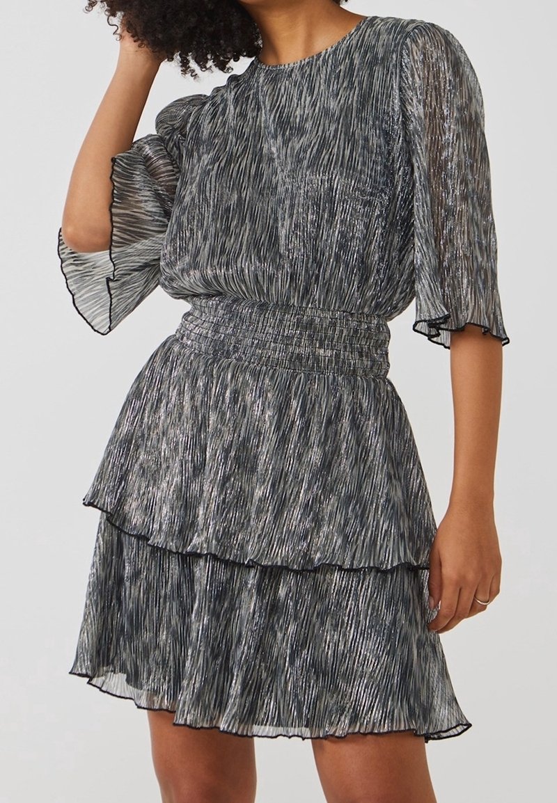 Femme portant une robe plissée à motifs argent métallisé et noir, avec des manches bouffantes et une taille cintrée.