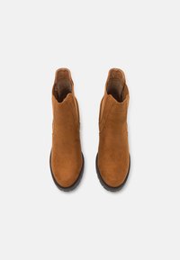 Brązowe botki zamszowe o gładkiej fakturze, zaokrąglonym nosku i elastycznych panelach bocznych. Gumowa podeszwa zapewniająca przyczepność i stabilność.