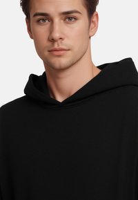 Sweatshirt à capuche noire avec une texture douce, une coupe décontractée et une capuche lisse. Design minimaliste sans motifs ni accents visibles.