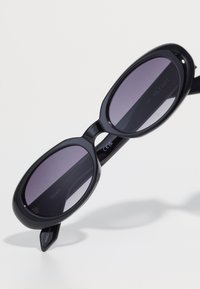 Óculos de sol pretos com lentes ovais, com tonalidade gradiente de roxo escuro, armações grossas e um design de dobradiça arrojado. Nome da marca gravado no lado interno do arco.