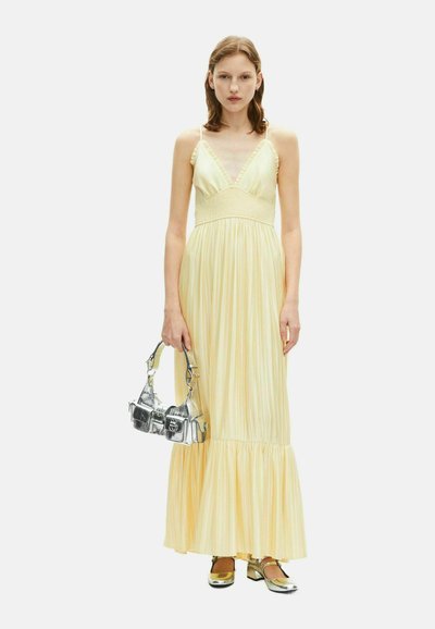 Abito maxi a righe gialle con scollatura a V, spalline arricciate e busto arricciato. Abbinato a una borsa argento e scarpe dorate lucide.