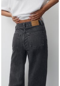 Mustat korkeavyötäröiset farkut, joissa haalistunut viimeistely, vyötäröllä vaaleanruskea nahkainen merkki ja klassiset takataskut.