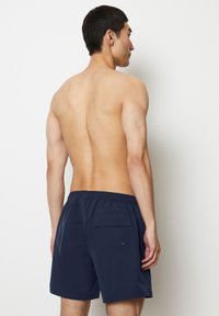 Marinblå badshorts med elastisk midja, enkel bakficka och slät textur. Designade för komfort och funktionalitet.