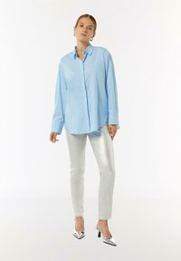 Light blue button-up shirt with long sleeves, paired with silver metallic skinny jeans and silver high-heeled shoes.