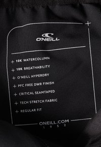 Zwarte stoffen label met witte tekst die kenmerken opsomt: 10K waterkolom, ademend, O'Neill Hyperdry, PFC-vrij DWR-finish, technische stretchstof.