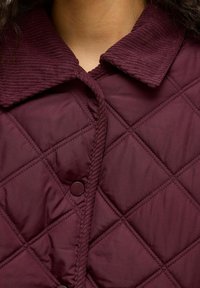 Burgundy quilted outerwear with a corduroy collar, featuring diamond patterns and rounded buttons, creating a textured look.