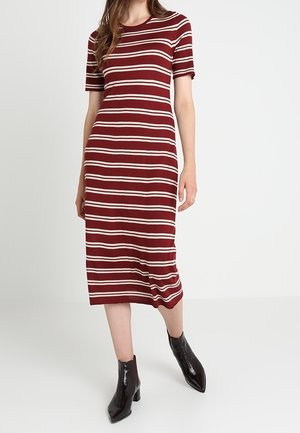 Frau trägt ein midi Kleid mit roten und weißen horizontalen Streifen, kurzen Ärmeln und schwarzen spitzen Stiefeletten.