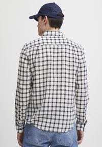 Rutete langermet skjorte i svart og hvit stoff med krage med knapper, buet underkant og mansjetterte ermer, brukt sammen med en marineblå caps.