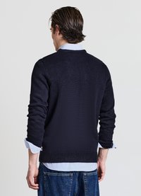 Marineblauer Strickpullover mit langen Ärmeln, strukturiertem Stoff, rundem Ausschnitt und geripptem Saum, getragen über einem hellblauen Hemd mit Kragen.