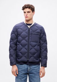 Μπλε σκούρο καπιτονέ μπουφάν με φερμουάρ μπροστά, κρεμ γιακά και τσέπη στο στήθος. Διαθέτει στρογγυλεμένα μοτίβα και κομψή, επενδυμένη υφή.