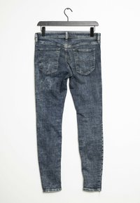 Jeans ajustados en denim azul oscuro con un acabado deslavado, que presentan una cintura de altura media y cinco bolsillos, colgando de una percha negra.