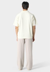 Krátký rukáv, texturovaná krémová košile s límečkem, zobrazená zezadu. Spárovaná se světle béžovými kalhotami s širokými nohavicemi.