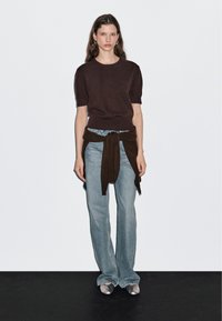 Bruine korte mouwen trui, geknoopte bruine stof om de taille, lichtblauwe flared denim jeans en zilveren gespschoenen.