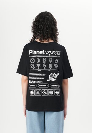 T-shirt noir avec du texte blanc et des symboles planétaires au dos. Coupe ample, manches courtes, avec un col rond et un design décontracté.