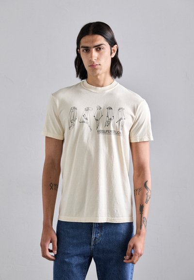 T-shirt en coton couleur crème à manches courtes, présentant un imprimé graphique de mains et le texte "KIDSUPER STUDIO" au centre.
