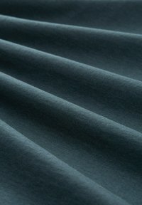 La tela color verde oscuro presenta una textura suave y lisa con un ligero brillo. La superficie muestra suaves pliegues y un patrón uniforme en toda su extensión.