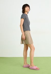 Stripet t-skjorte med korte ermer i marineblå og hvit, beigefarget plisserte skjørt, og rosa sandaler, stående på en grønn teppeoverflate.