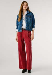 Džinsu jaka ar zilu mazgāšanu, balta krekliņa, sarkanas korduroja platās bikses, melna josta un melni smaili potīšu zābaki.