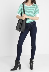 Grön- och vitrandig t-shirt med korta ärmar, mörkblå skinny jeans, svarta klackade ankel boots med spänne, och en svart tote-väska.