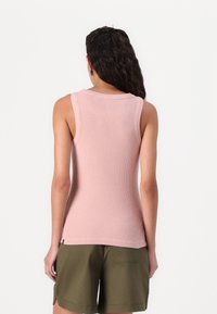 Hellrosa, gerippter Tanktop mit rundem Ausschnitt und ärmellosem Design, kombiniert mit olivgrünen Shorts. Sichtbare Nähdetails an den Kanten.