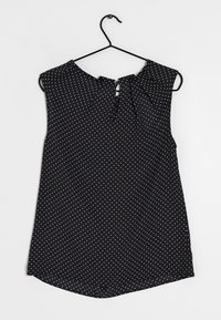 Top senza maniche nero con pois bianchi, caratterizzato da un'apertura a chiave sul retro e una vestibilità rilassata, realizzato in tessuto leggero.