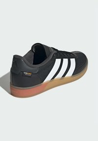Black sneaker with white stripes, made from Cordura fabric and synthetic materials. Features a rubber sole with a transparent edge and logo.