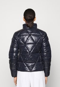 Mörkblå puffjacka med en glansig finish, med ett diamantquiltat mönster, hög krage och långa ärmar.