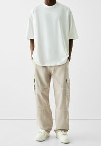 Vit oversized t-shirt med rund halsringning, tillsammans med beige cargo-byxor med sidofickor och manschetter, komplett med vita sneakers.