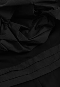 Crna tkanina s slojevitim volanima i glatkom teksturom; sadrži horizontalne nabore duž donjeg dijela, stvarajući dubinu i pokret.