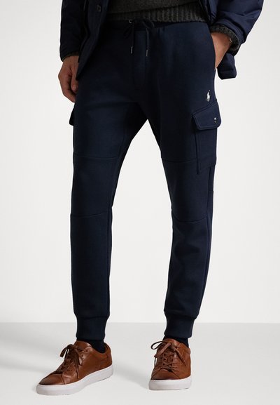 Meripihkaväriset sweatpants pehmest kankaast, varustettu sivukargo-taskut, ribbi-hihansuut ja kiristysnauha vyötäröllä. Yhdistetty ruskeisiin lenkkareihin.
