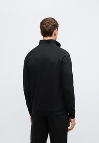 Μαύρο πουλόβερ με μακριά μανίκια και ψηλό γιακά, με λεία υφή και ριμπ τελείωμα. Λεπτομέρειες ραφής στα μανίκια. Ανεπίσημη εφαρμογή.