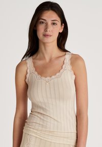 Beige tanktop met verticale strepen, kantafwerking aan de hals en banden, zachte stof, aansluitende vorm en decoratieve strikdetail in het midden.